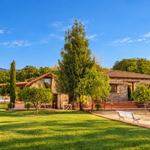 Vista de la finca con la casa de piedra, el porche y el jardín de césped – casa rural Aprisco de Candeleda (Ávila)