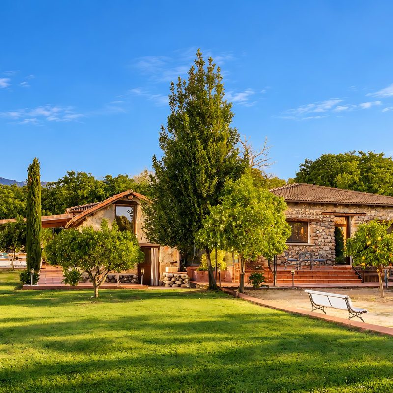 Vista de la finca con la casa de piedra, el porche y el jardín de césped – casa rural Aprisco de Candeleda (Ávila)