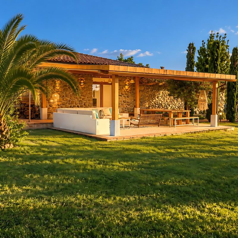 Porche cubierto de la casa entre palmeras y césped – casa rural Aprisco de Candeleda (Ávila)